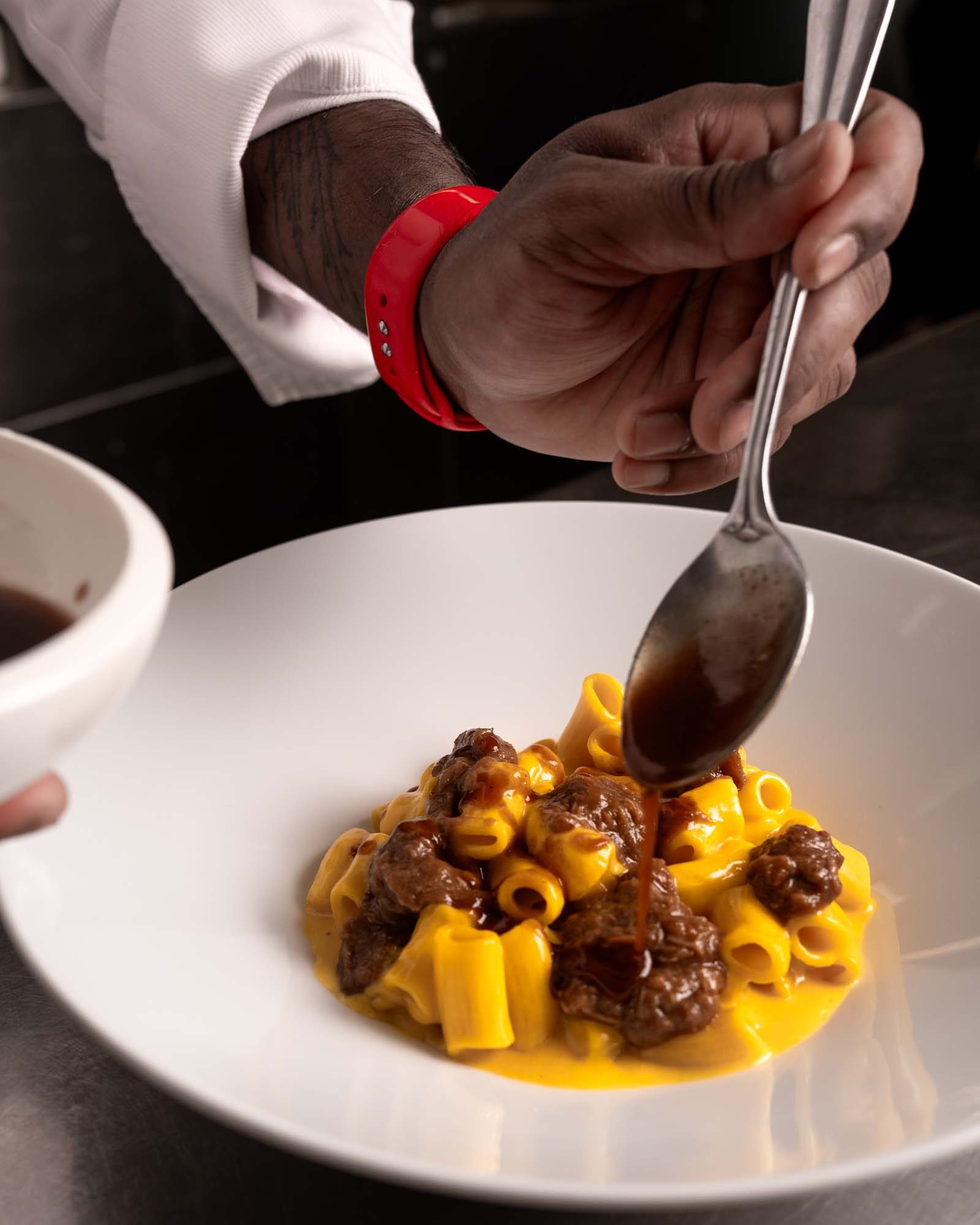 Chef versa salsa su pasta al ragù di carne in piatto bianco