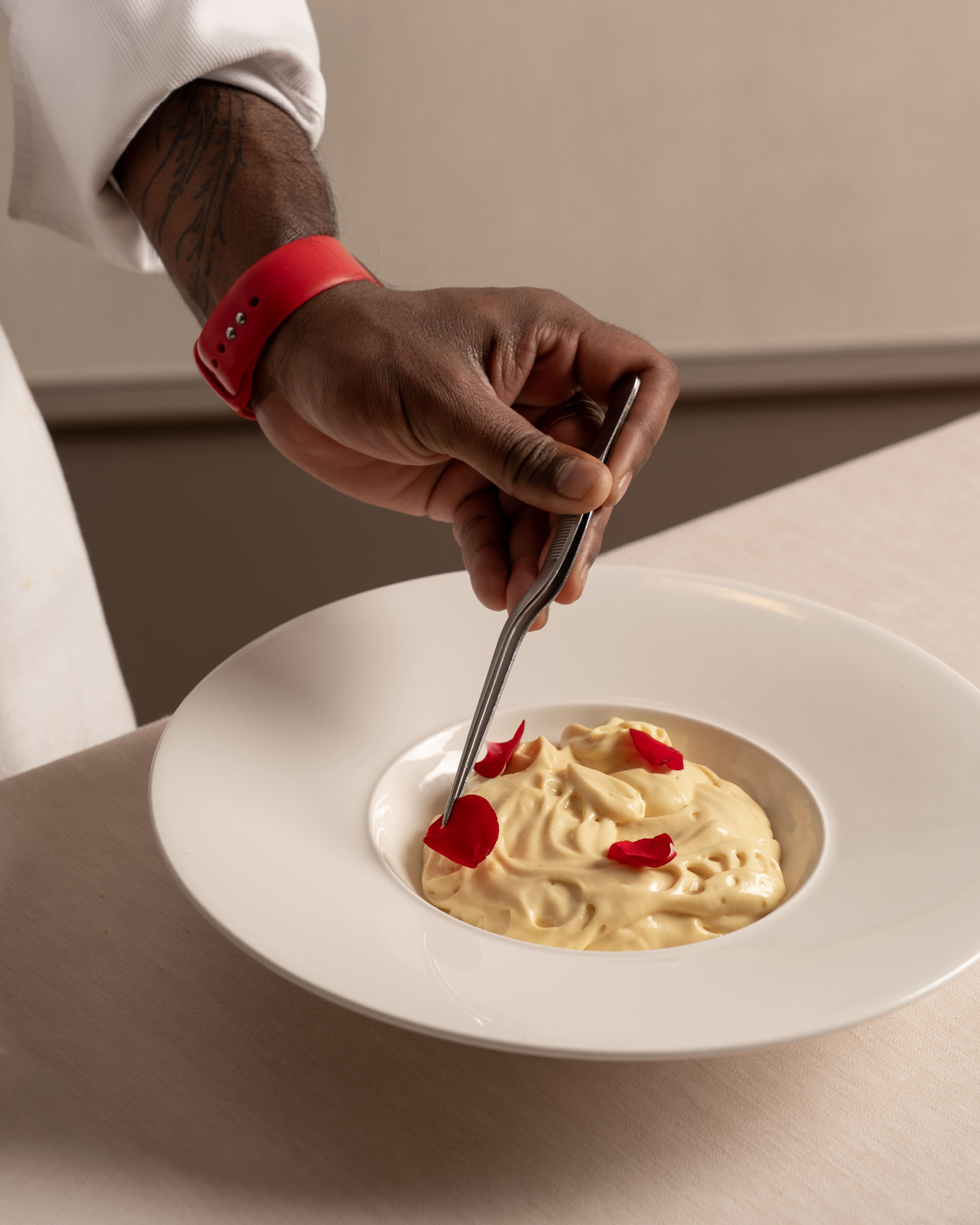 mano di chef con pinzette che decora crema soffice con petali di rosa