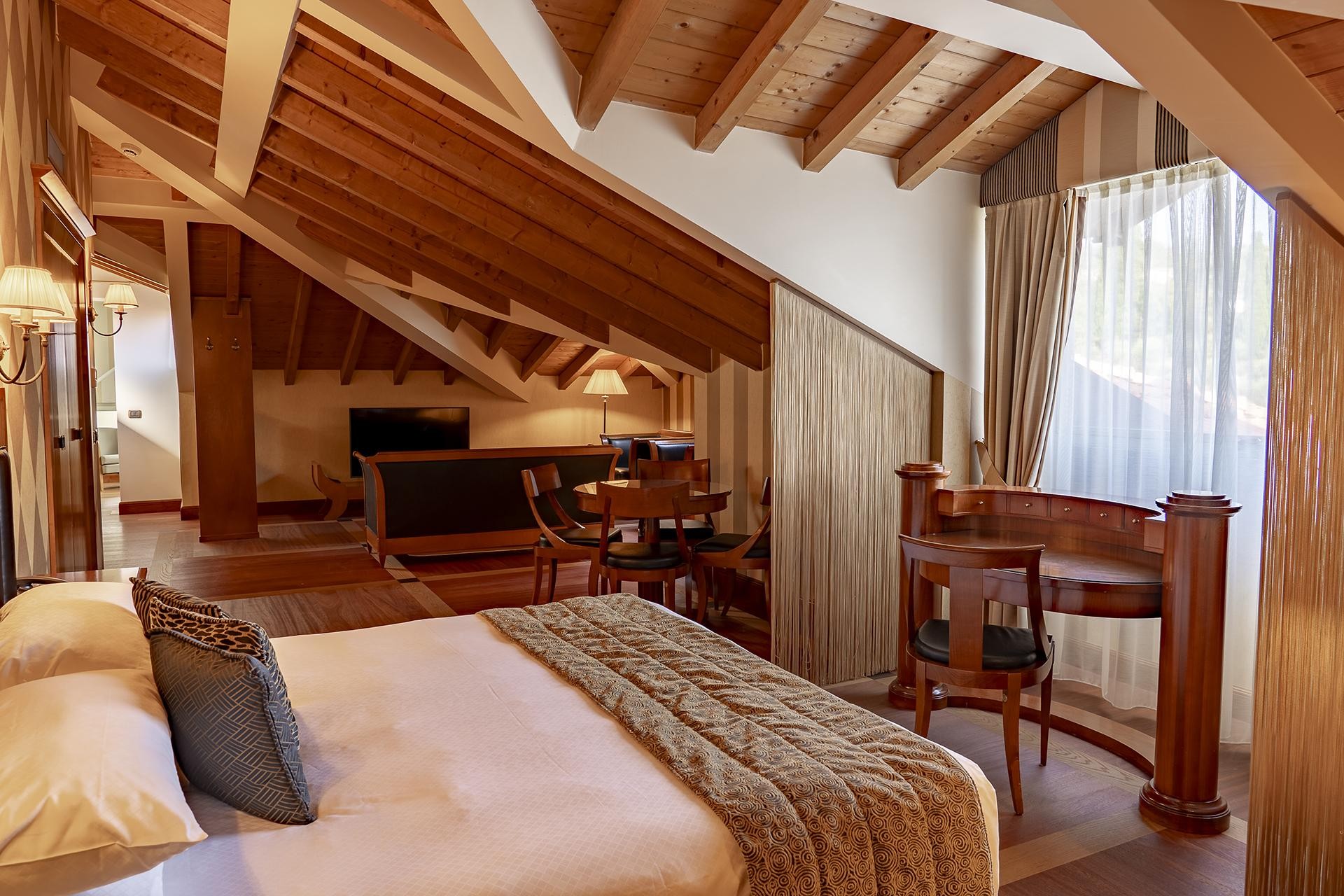 Gemütliche Dachgeschoss-Suite mit Sichtbalken, Bett und Schreibtisch am Fenster.