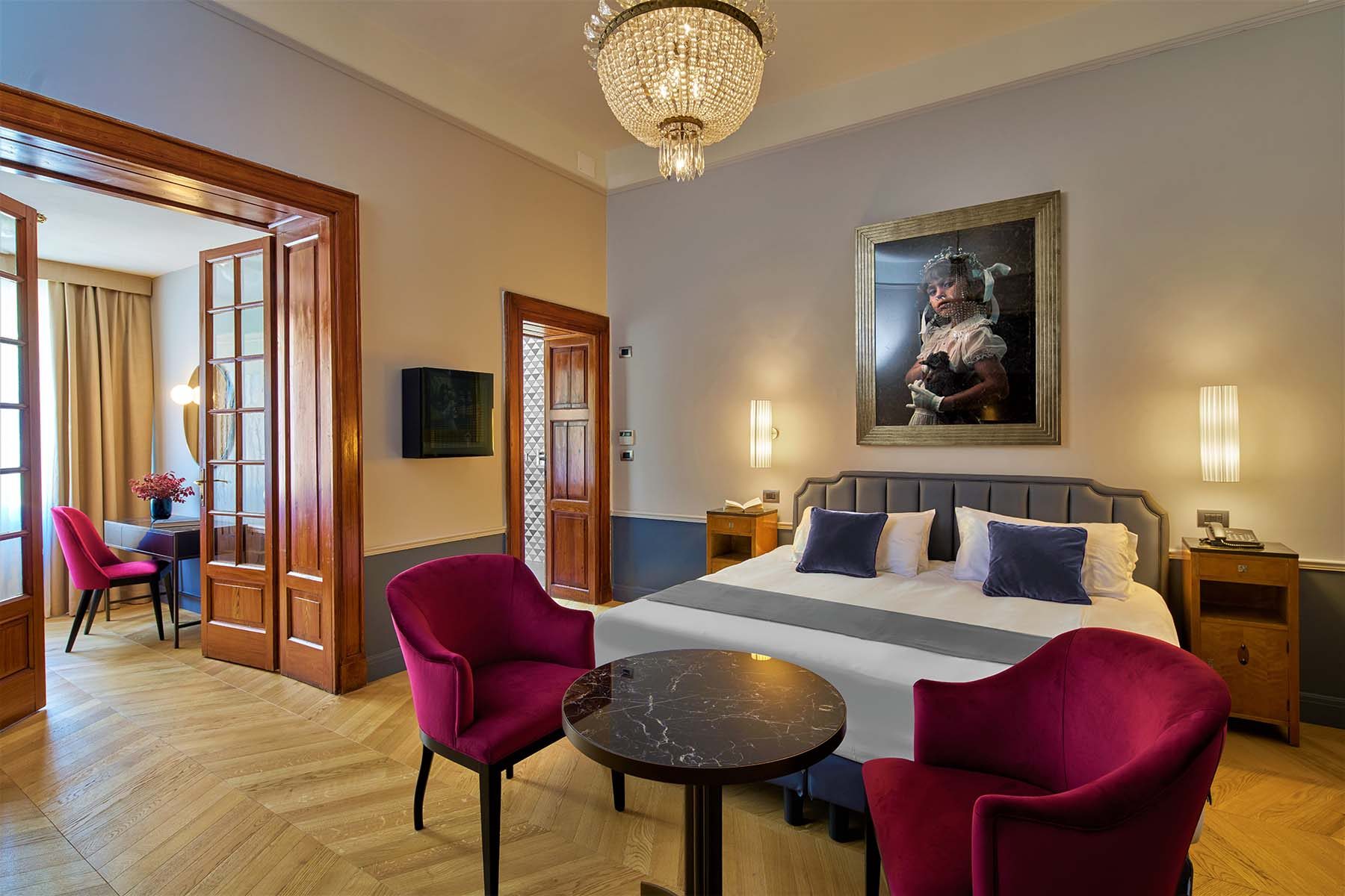 Elegantes Hotelzimmer mit Doppelbett, Samtsesseln in Magenta und Kronleuchter