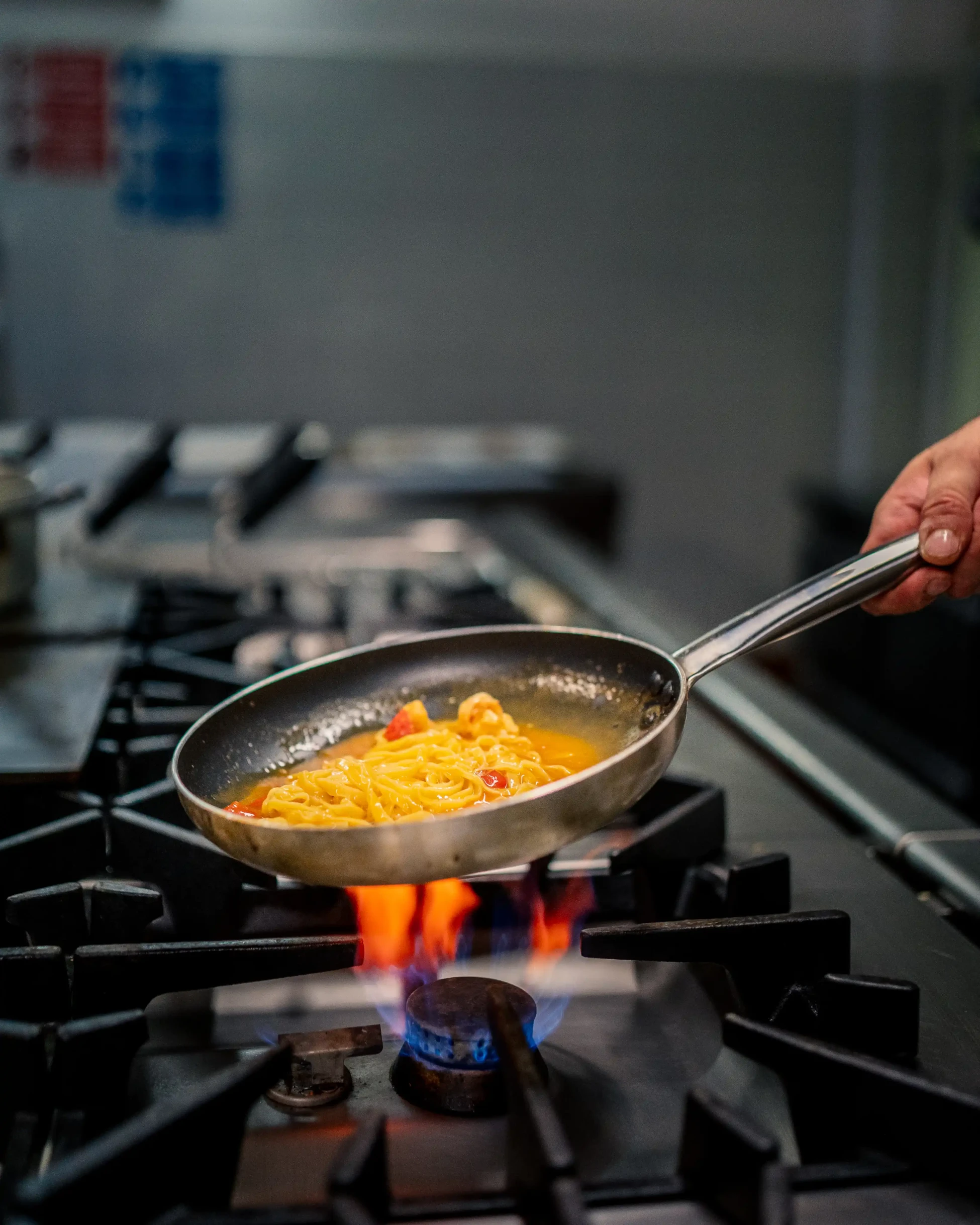 Pfanne mit Pasta in Sauce auf Gasherdflamme.