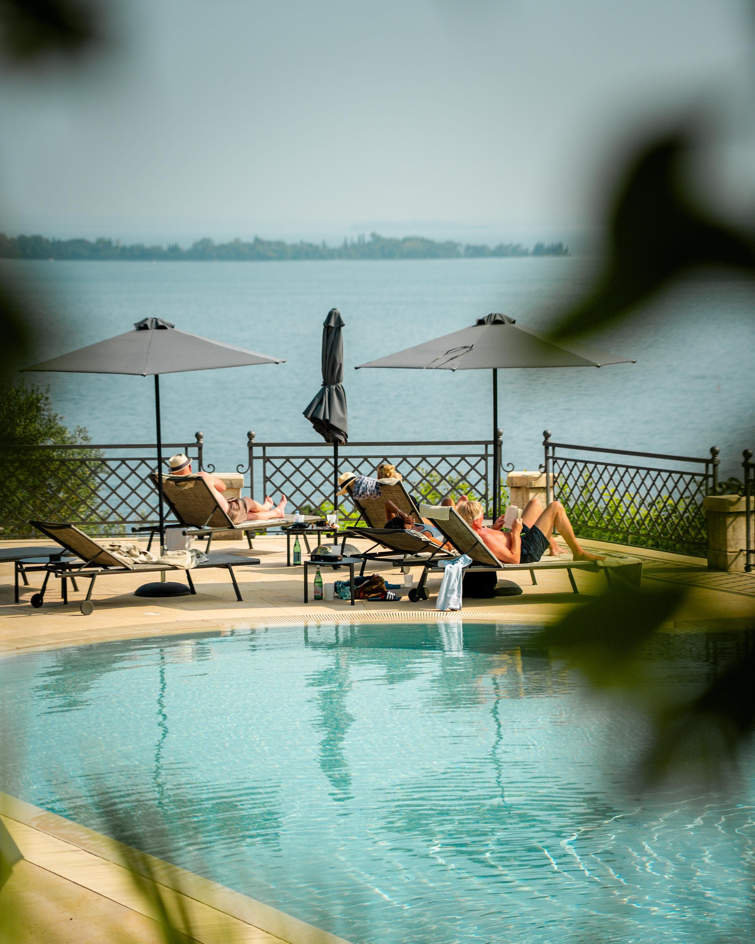 Pool am See mit Liegestühlen und Sonnenschirmen, entspannter Urlaub.