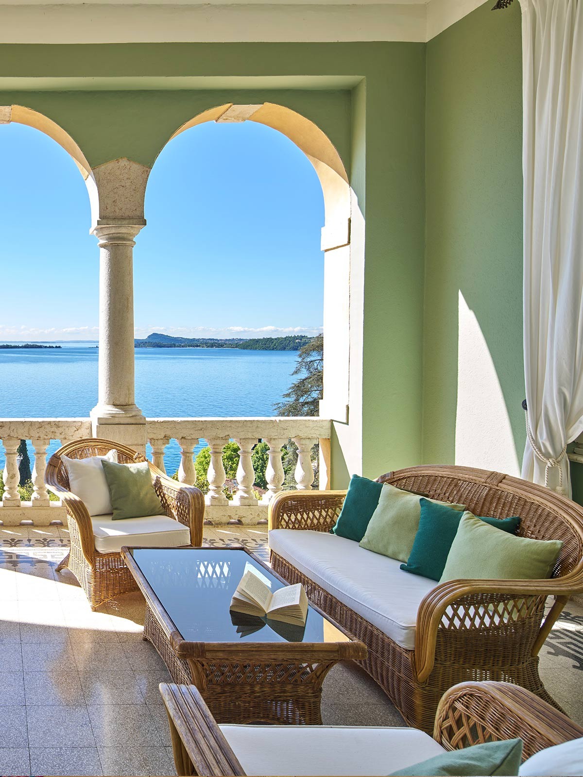 Seeterrasse mit Rattansofa, Arkaden und Glastisch mit Buch