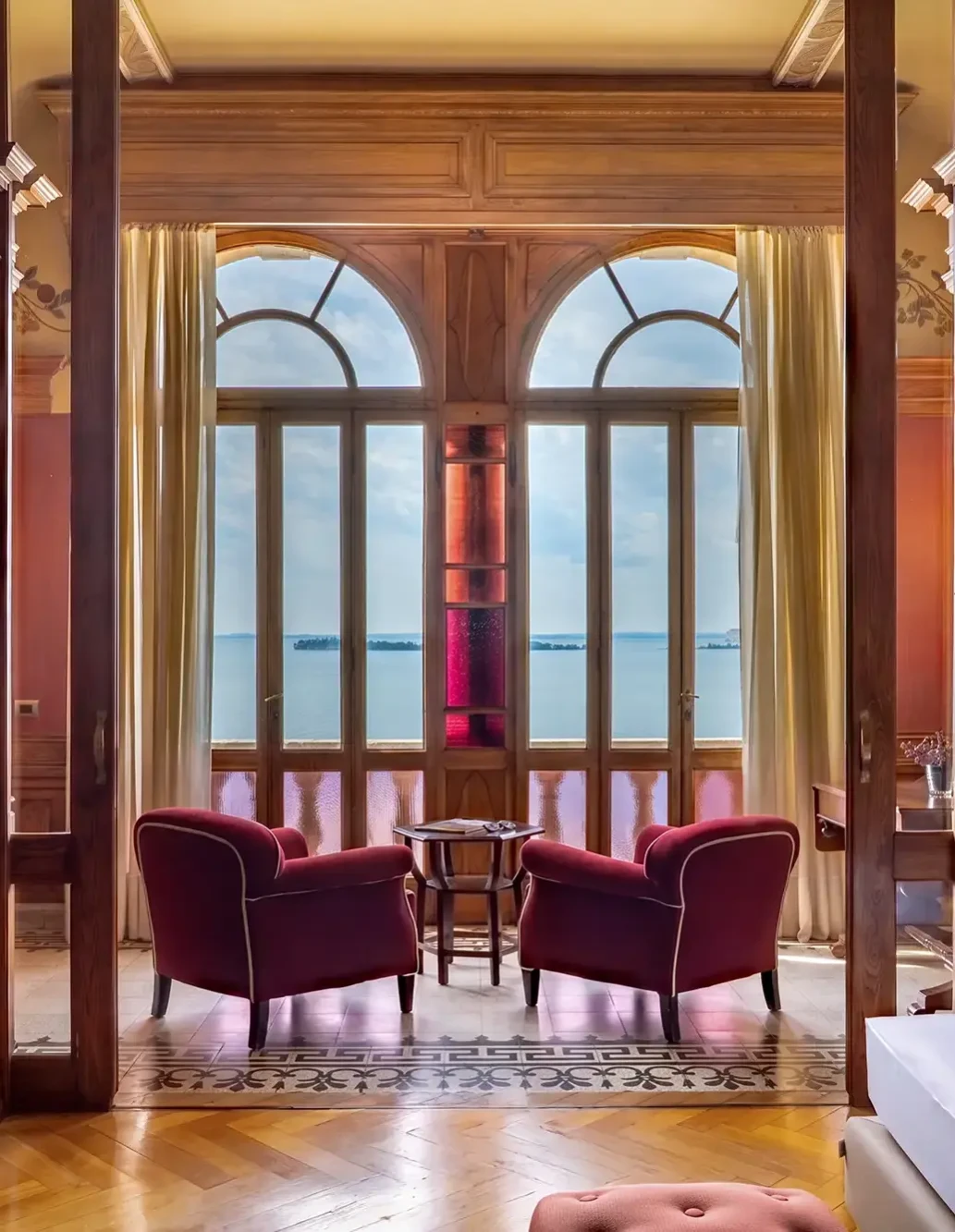 Elegantes Interieur mit zwei Sesseln und Tisch, Seeblick durch große Bogenfenster