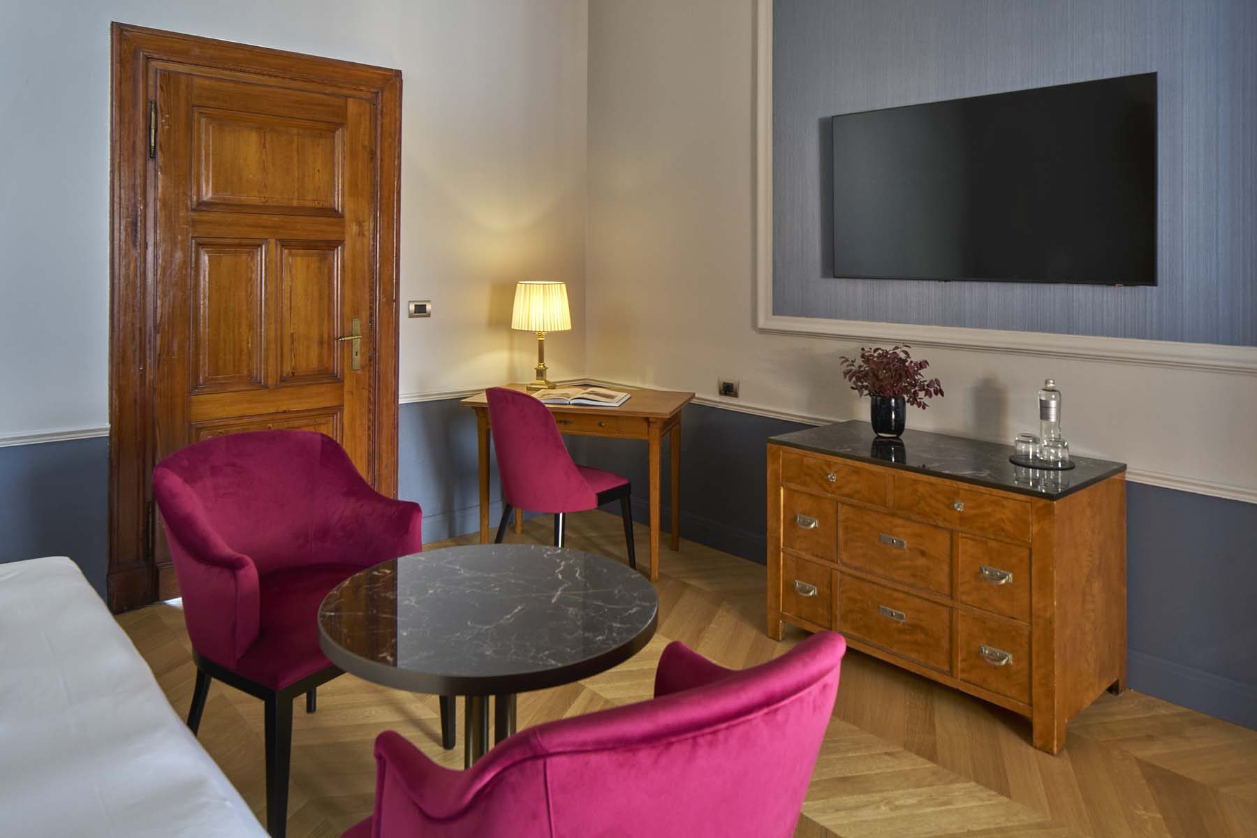 Stilvoller Sitzbereich mit pinken Samtsesseln, Marmortisch, Schreibtisch und Wandfernseher.