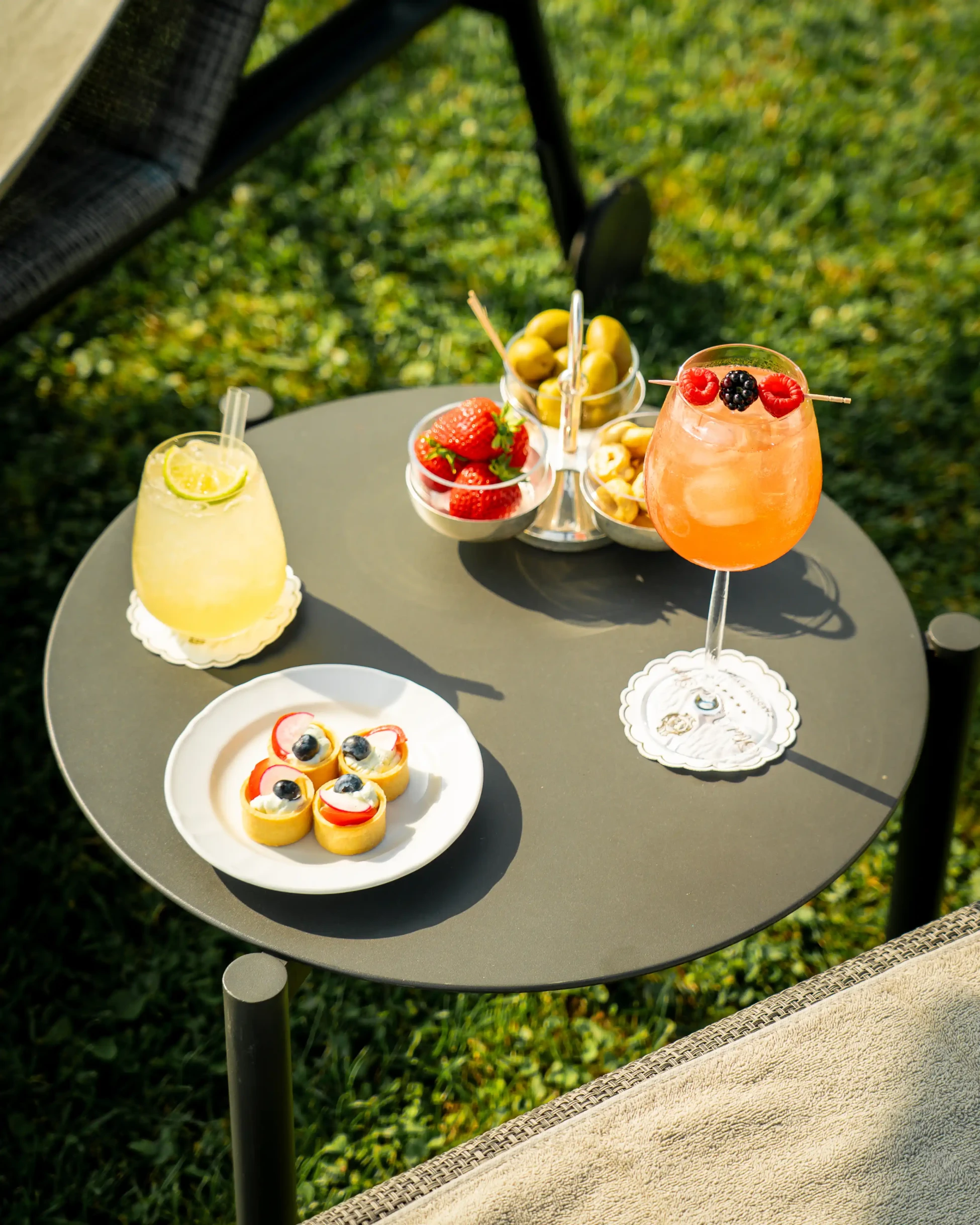 Zwei Sommercocktails mit Beeren, Obsttörtchen, Oliven und Erdbeeren auf Gartentisch